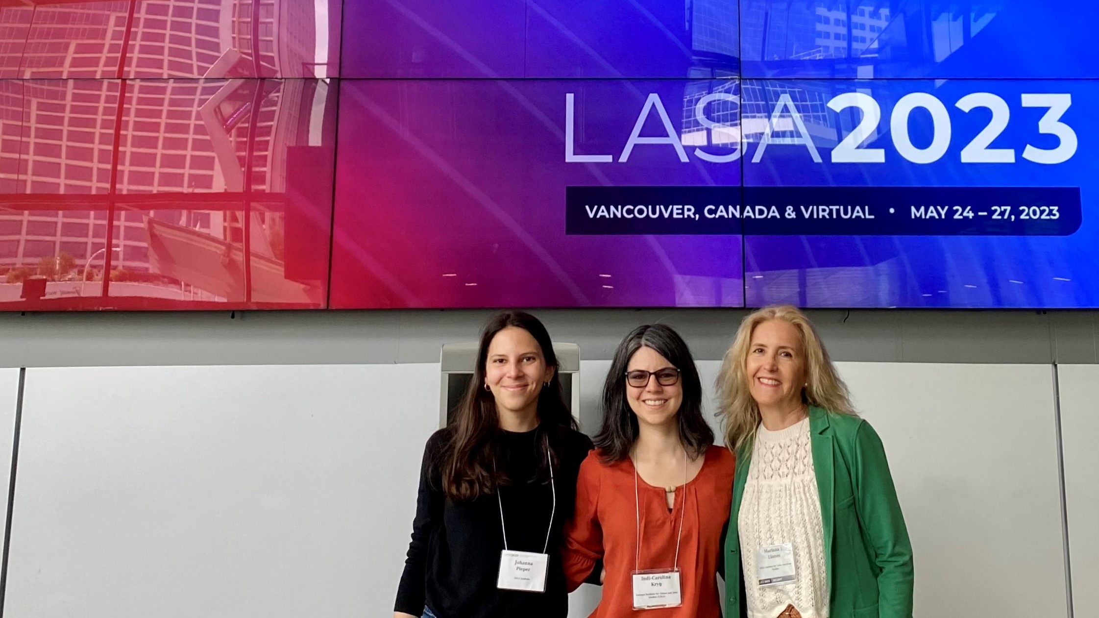 GIGA researchers Johanna Pieper, Indi-Carolina Kryg and Mariana Llanos standing infront of a screen promoting LASA Congress 2023.