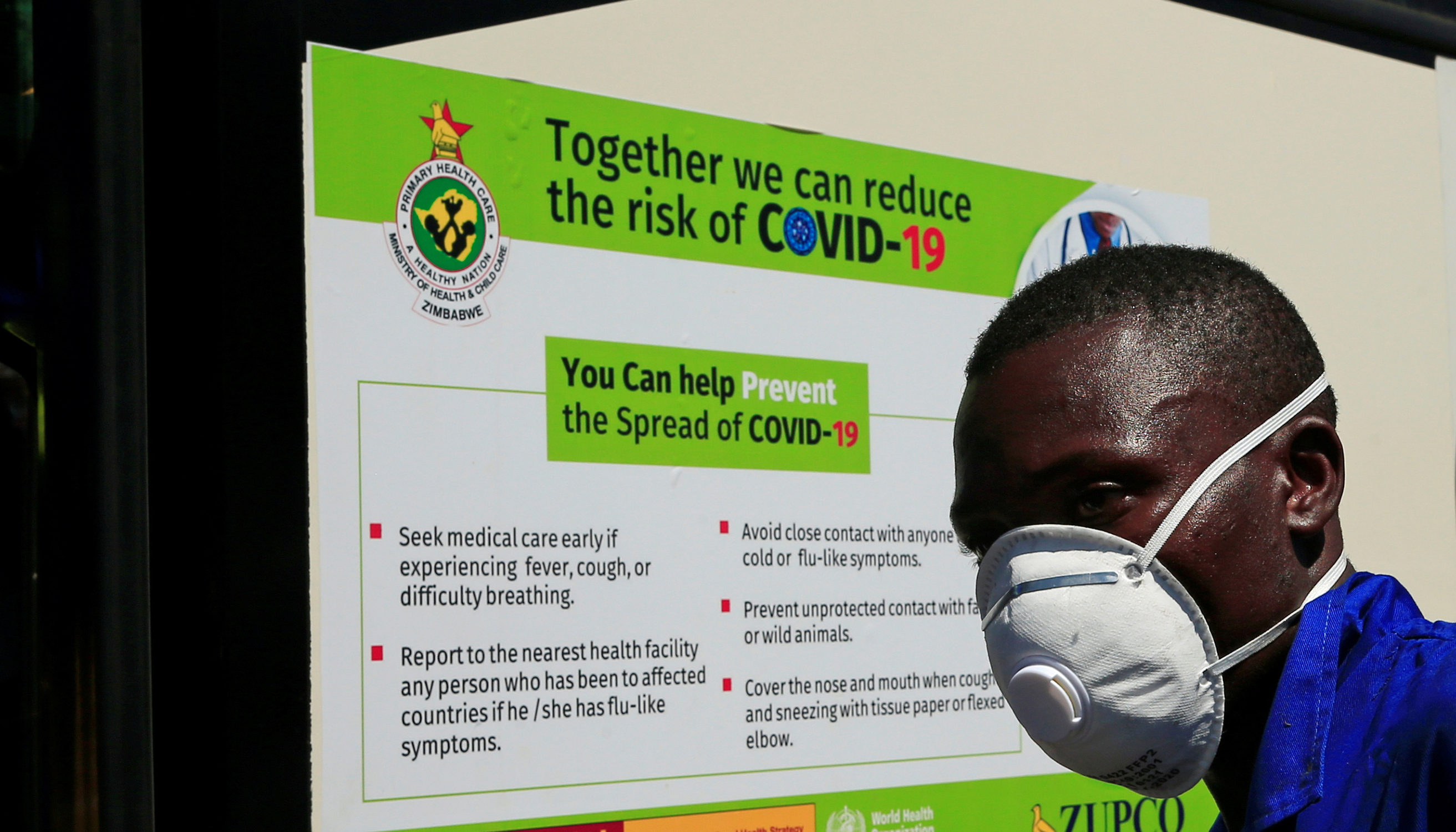 Ein Mann mit FSP-Maske steht vor einem Schild mit Verhaltensweisen zur Eindämmung des Coronsviruses.